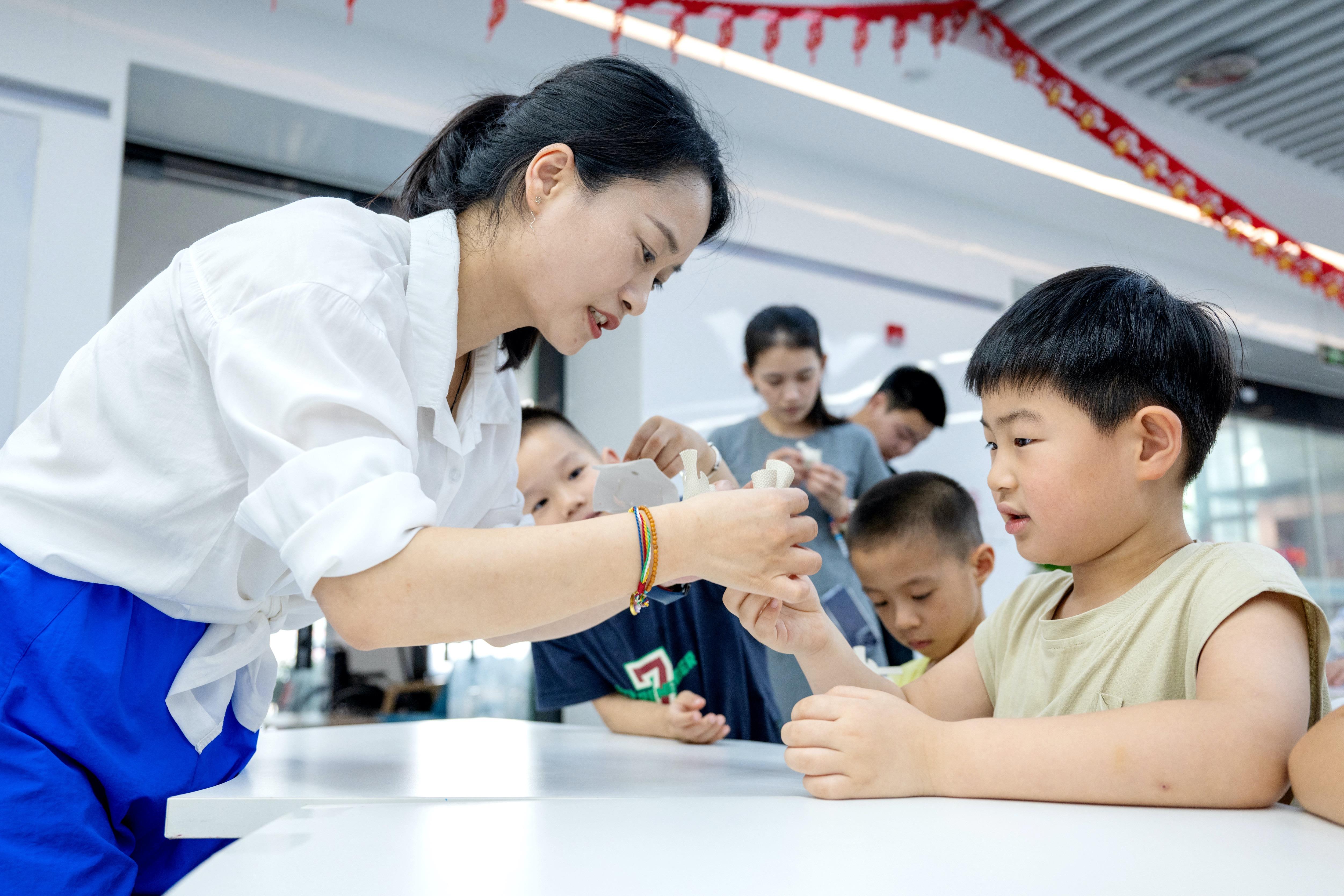 △2025年7月3日,浙江湖州长兴县龙山街道齐北社区幸福邻里中心,志愿者指导孩子们制作手工。